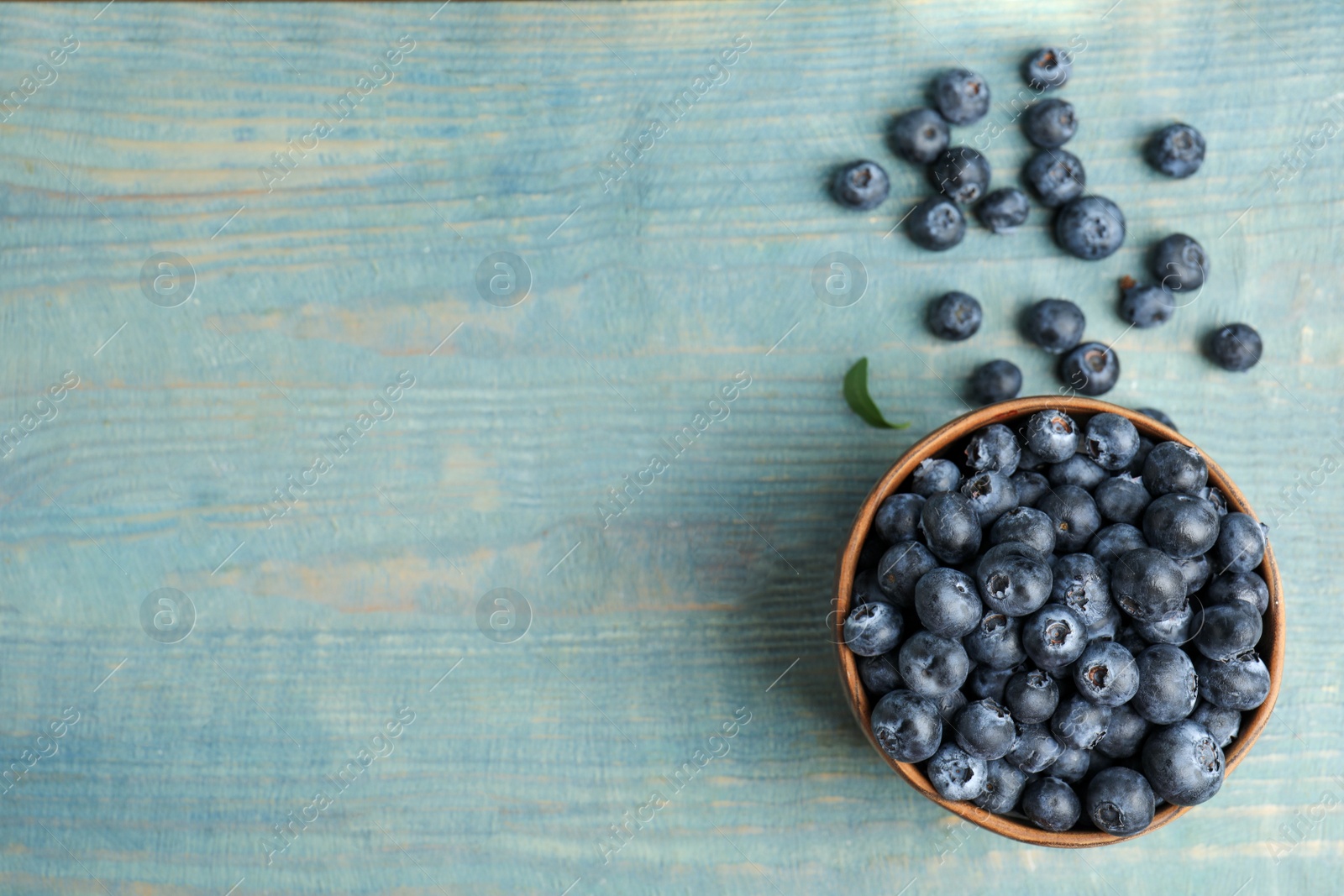 Photo of Fresh ripe blueberries in bowl on wooden table, flat lay. Space for text