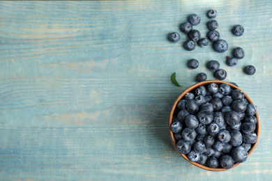 Fresh ripe blueberries in bowl on wooden table, flat lay. Space for text