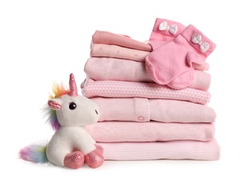 Photo of Stack of baby girl's clothes, socks and toy unicorn on white background