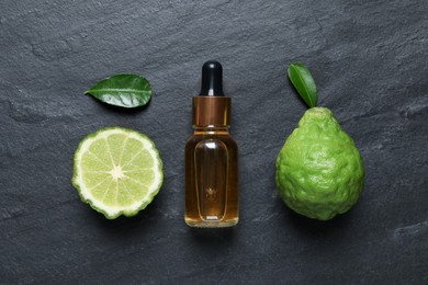 Photo of Glass bottle of bergamot essential oil and fresh fruits on black slate table, flat lay