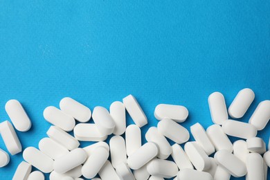 Photo of Vitamin pills on light blue background, top view. Space for text