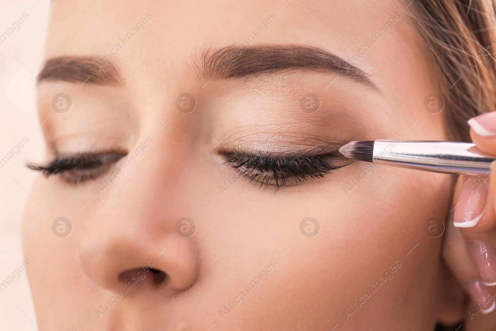Photo of Professional visage artist applying makeup on woman's face in salon, closeup