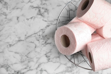 Photo of Bowl with toilet paper rolls on marble background, top view. Space for text