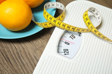 Photo of Scales, measuring tape and oranges on wooden background, closeup. Weight loss