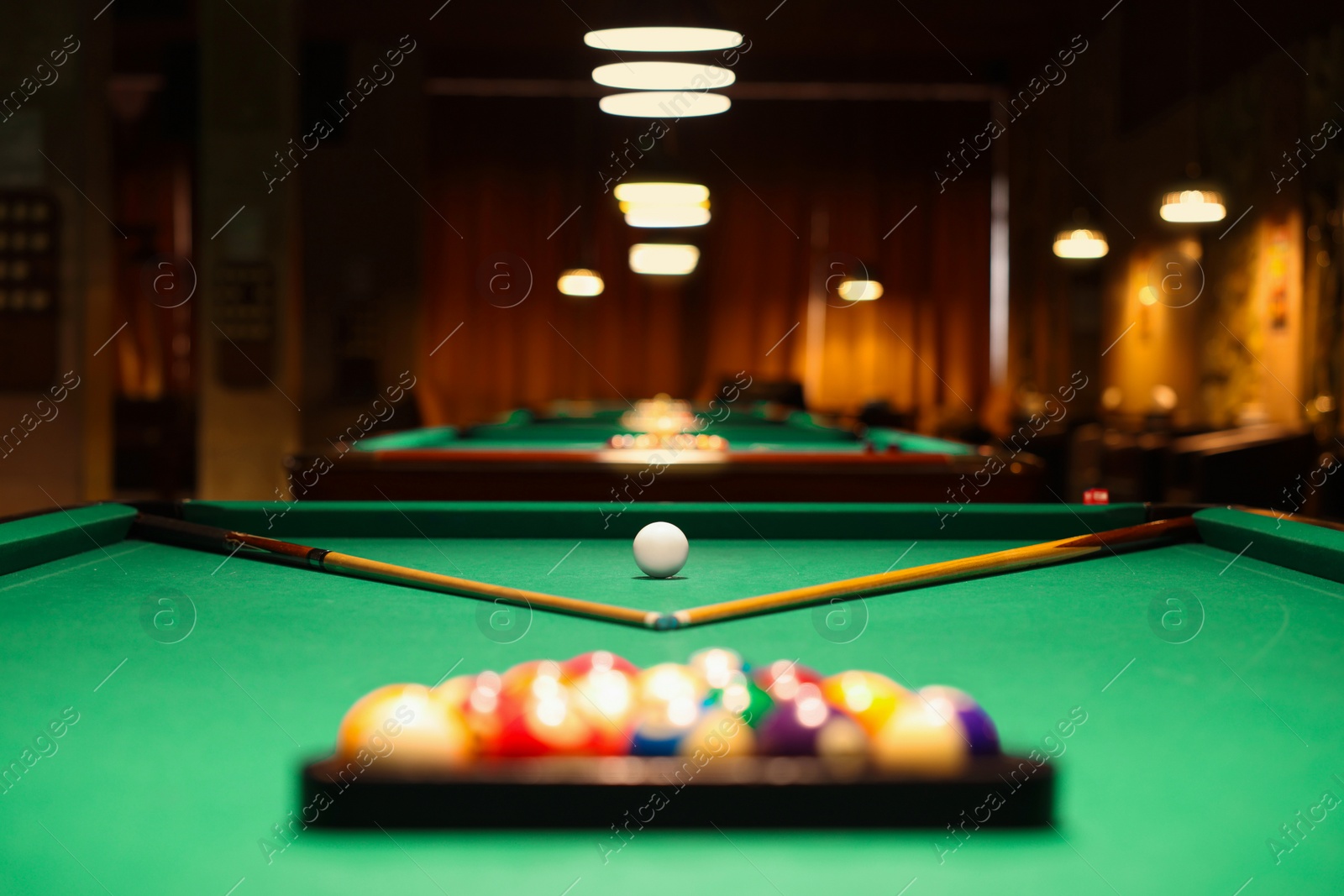 Photo of Plastic triangle rack with billiard balls and cues on green table indoors, selective focus