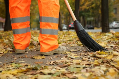 Street cleaner sweeping fallen leaves outdoors on autumn day