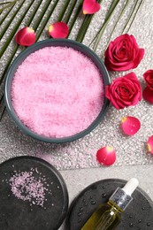 Photo of Natural sea salt in bowl, spa stones, cosmetic product, rose flowers and petals on grey table, flat lay