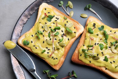 Delicious sandwiches with guacamole, seeds and microgreens on black plate, top view