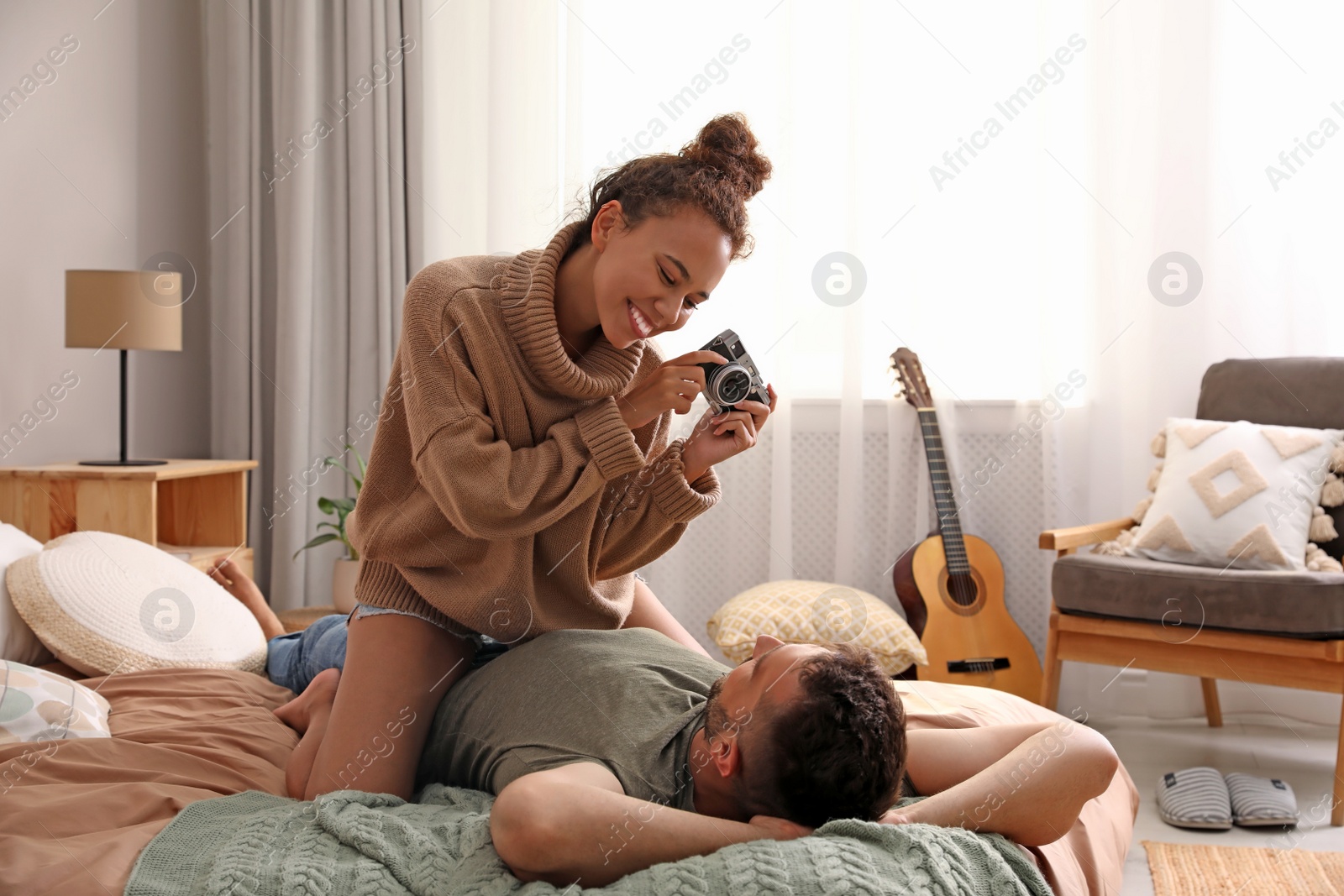 Photo of Beautiful African-American woman taking picture of her boyfriend on bed at home