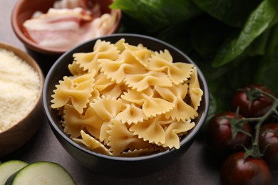 Photo of Raw pasta, bacon and fresh ingredients on brown table