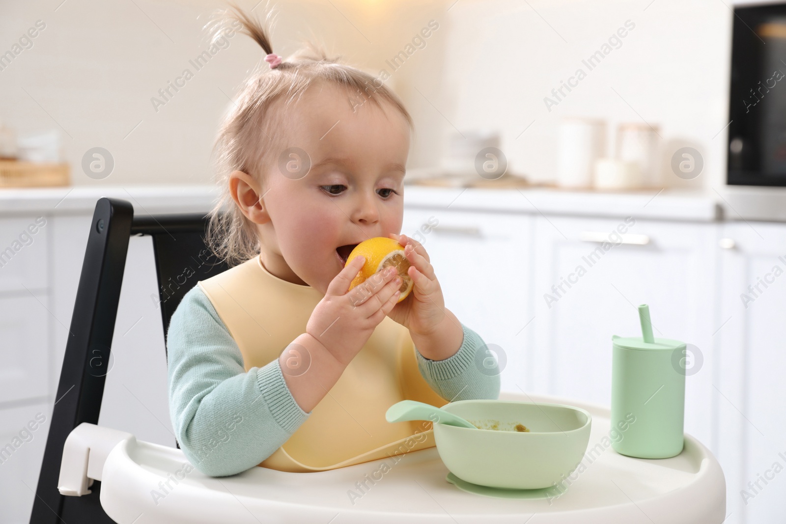 Photo of Cute little baby with lemon in high chair at kitchen