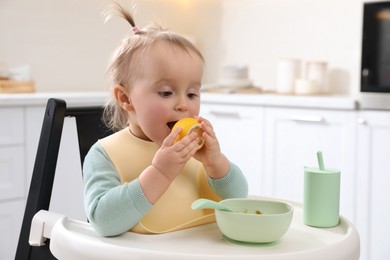 Photo of Cute little baby with lemon in high chair at kitchen