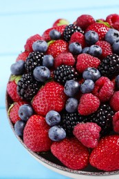 Photo of Different fresh ripe berries in bowl on light blue table, closeup