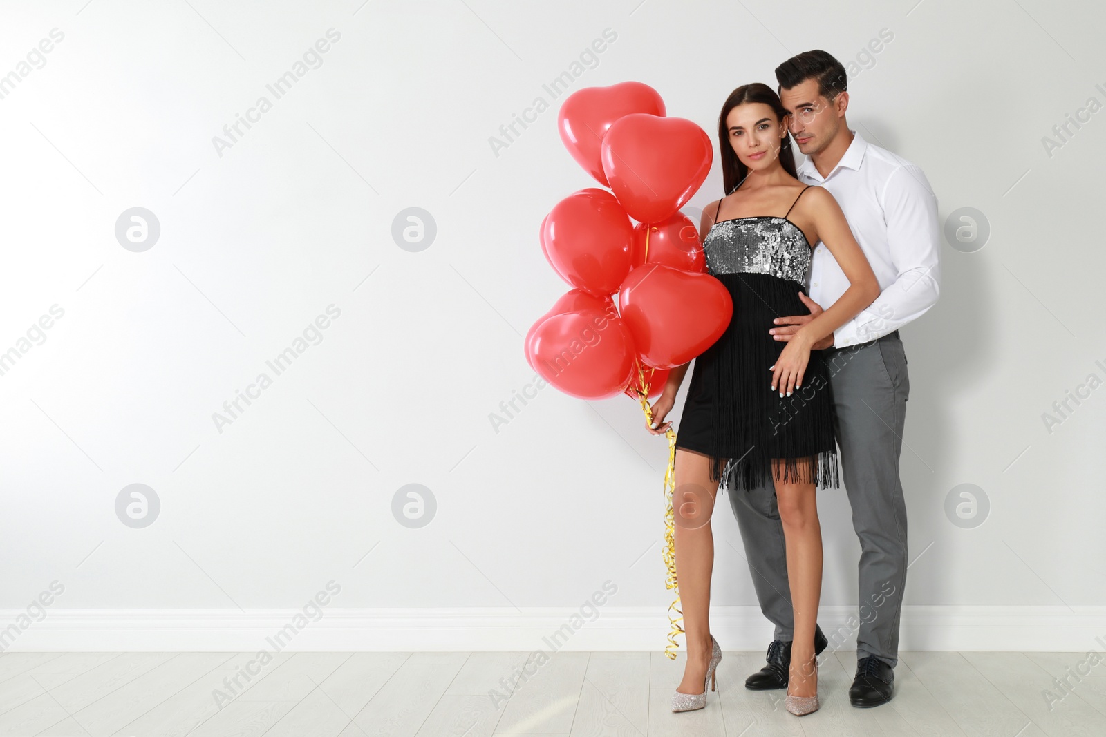 Photo of Beautiful couple with heart shaped balloons near light wall, space for text