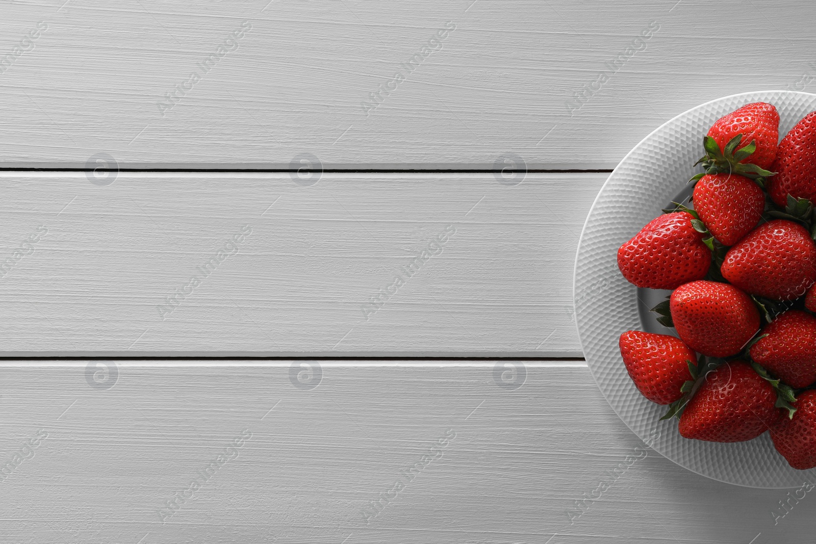 Photo of Food photography. Plate of delicious ripe strawberries on white wooden table, top view with space for text