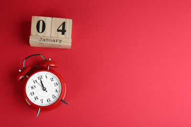 Photo of Wooden block calendar and alarm clock on red background, flat lay. Space for text