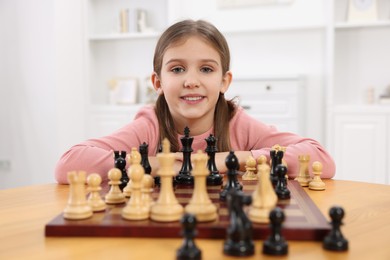 Cute girl playing chess at table in room