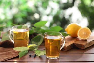 Cups of tasty iced tea with lemon on wooden table against blurred background