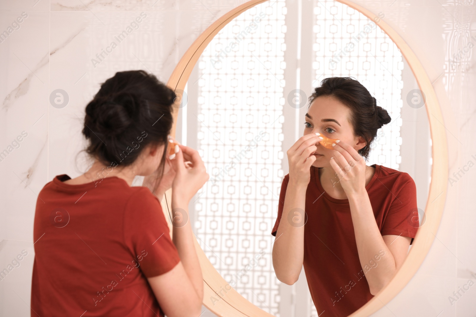 Photo of Young woman with eye patches near mirror in bathroom