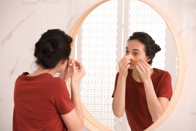 Photo of Young woman with eye patches near mirror in bathroom