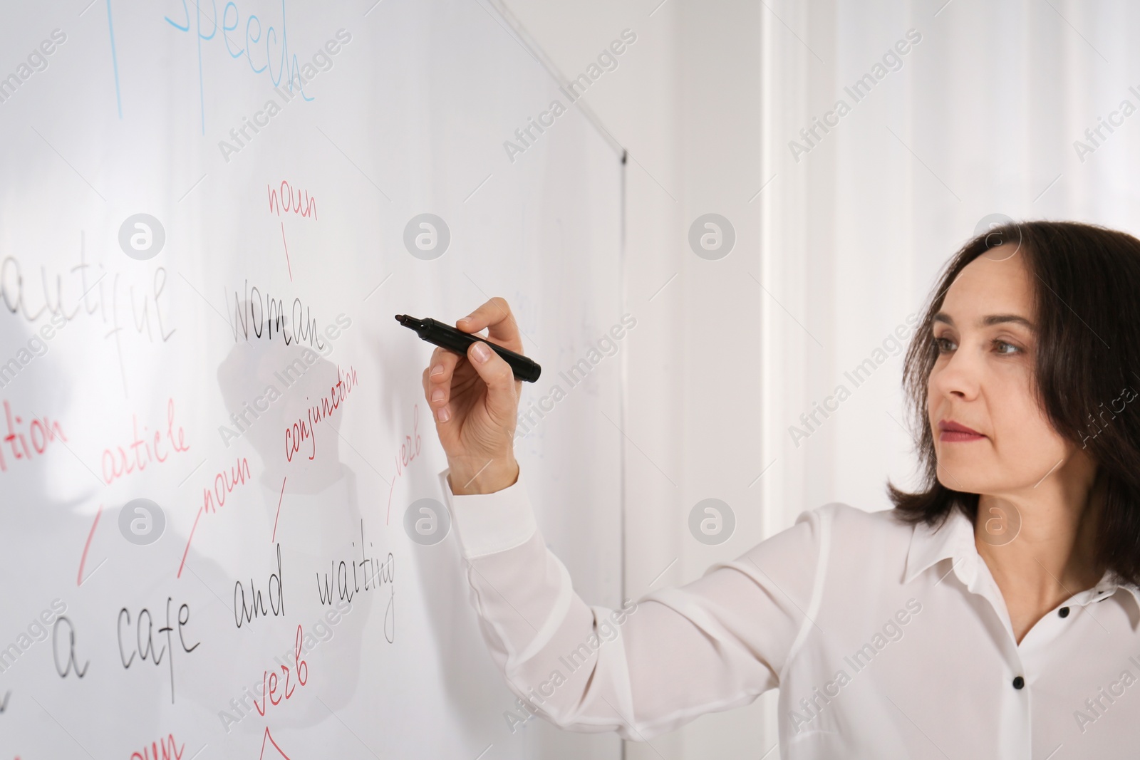 Photo of English teacher giving lesson near whiteboard in classroom