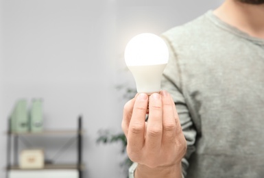 Photo of Man holding lamp bulb on blurred background, closeup with space for text