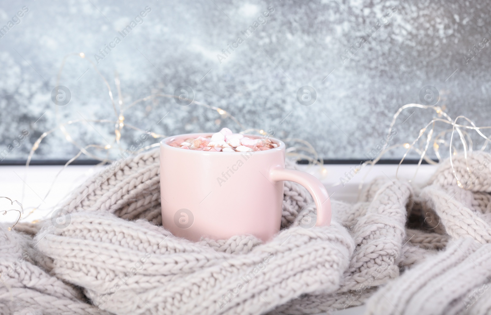 Photo of Cup of aromatic cacao with marshmallows and   warm scarf on window sill