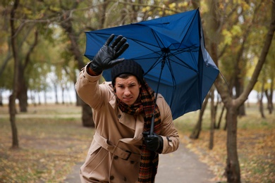 Man with blue umbrella caught in gust of wind outdoors