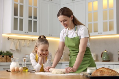 Photo of Making bread. Mother and her daughter rolling dough at wooden table in kitchen