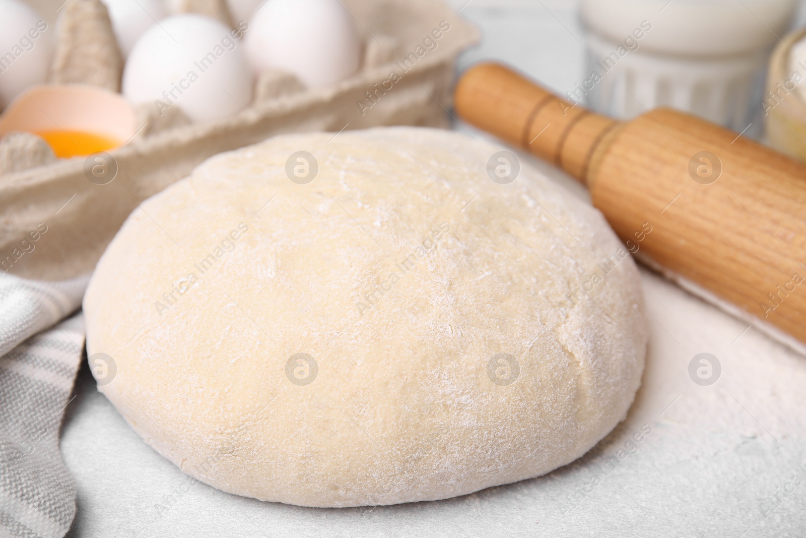 Photo of Dough, rolling pin and ingredients on white table, closeup