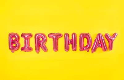 Word BIRTHDAY made of pink foil balloons letters on yellow background
