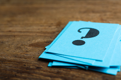 Photo of Blue paper cards with question mark on wooden background, closeup