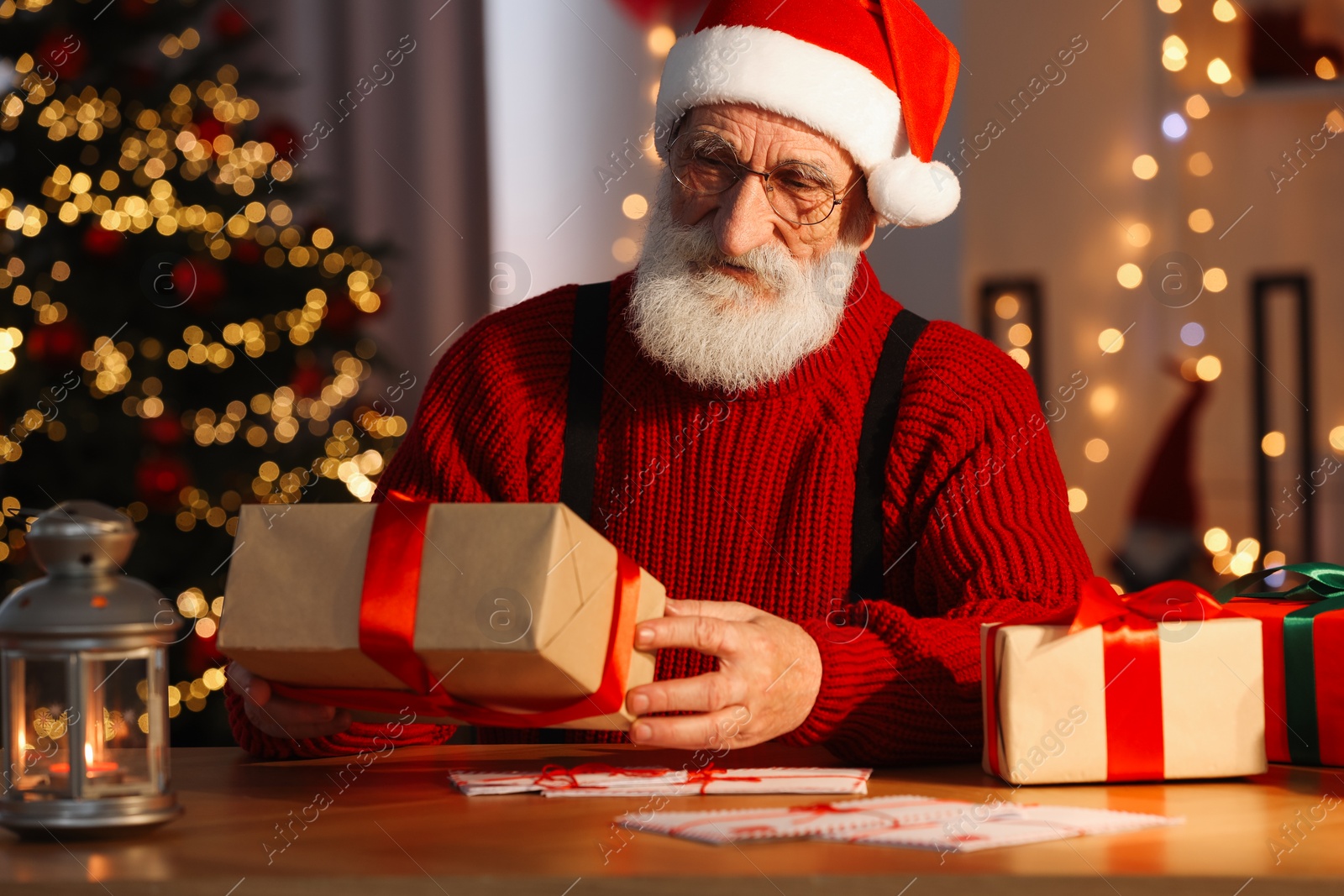 Photo of Santa Claus holding gift box at his workplace in room decorated for Christmas
