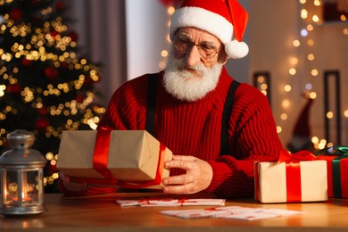 Santa Claus holding gift box at his workplace in room decorated for Christmas