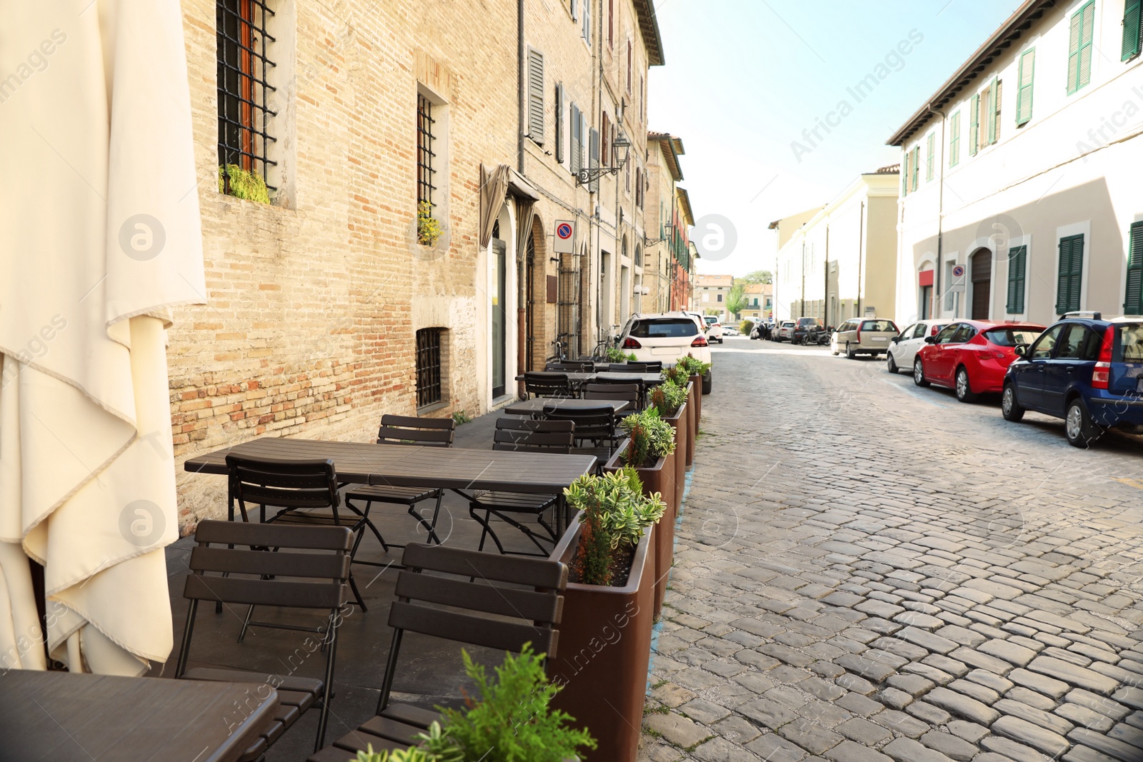 Photo of City street with tables and chairs near building. Outdoor cafe