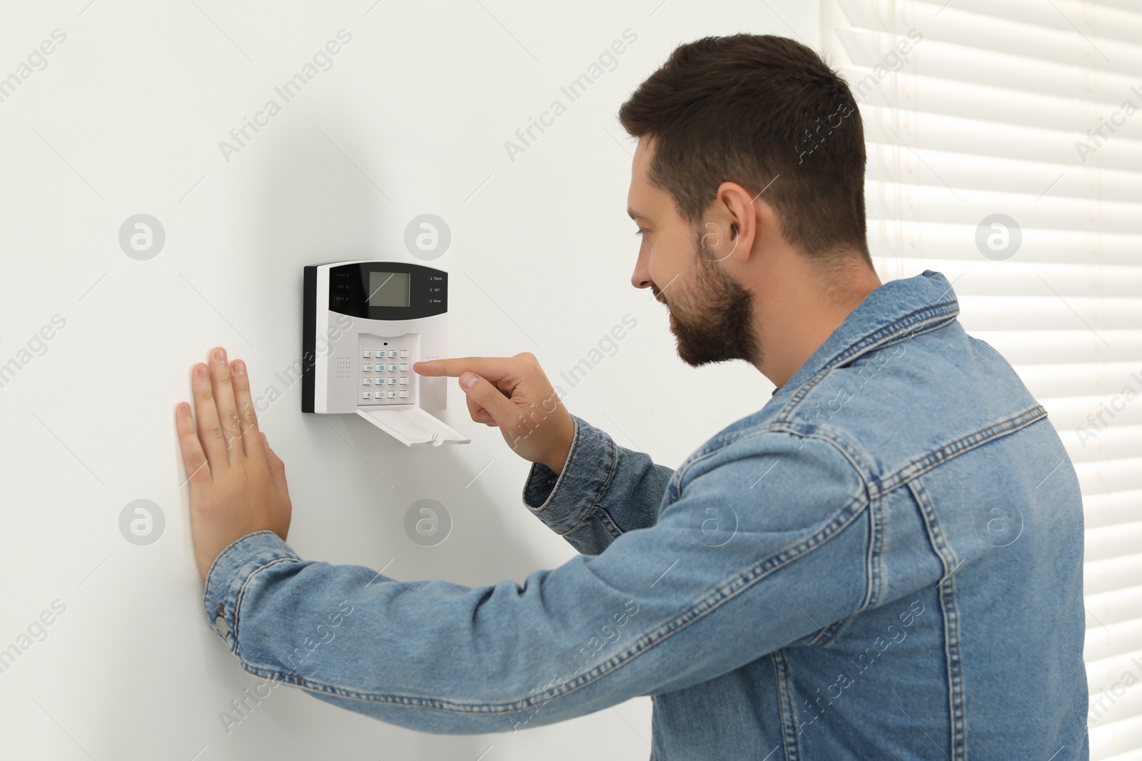 Photo of Man entering code on home security system indoors