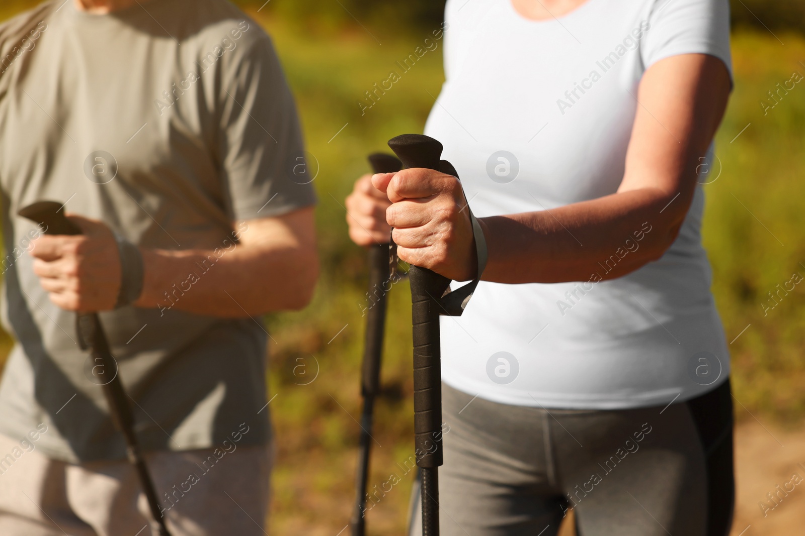 Photo of Couple practicing Nordic walking with poles outdoors on sunny day, closeup