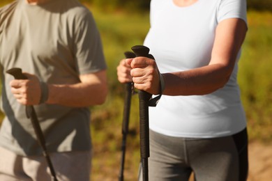 Couple practicing Nordic walking with poles outdoors on sunny day, closeup