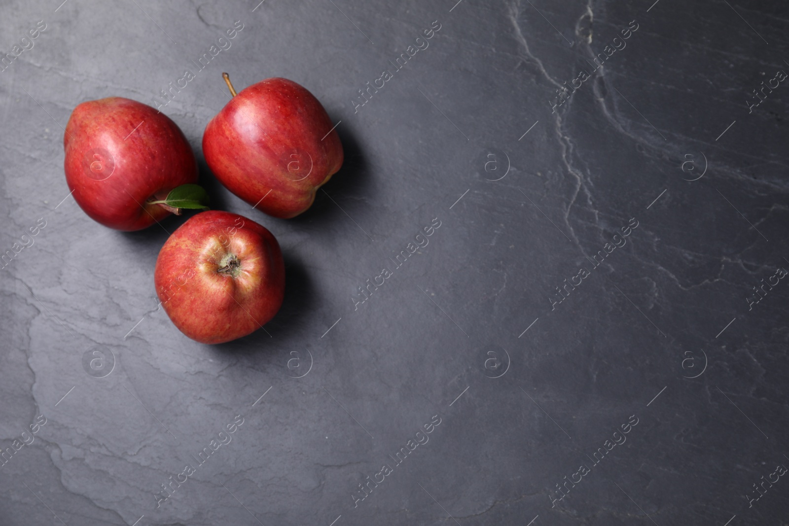 Photo of Ripe red apples on black textured table, flat lay. Space for text