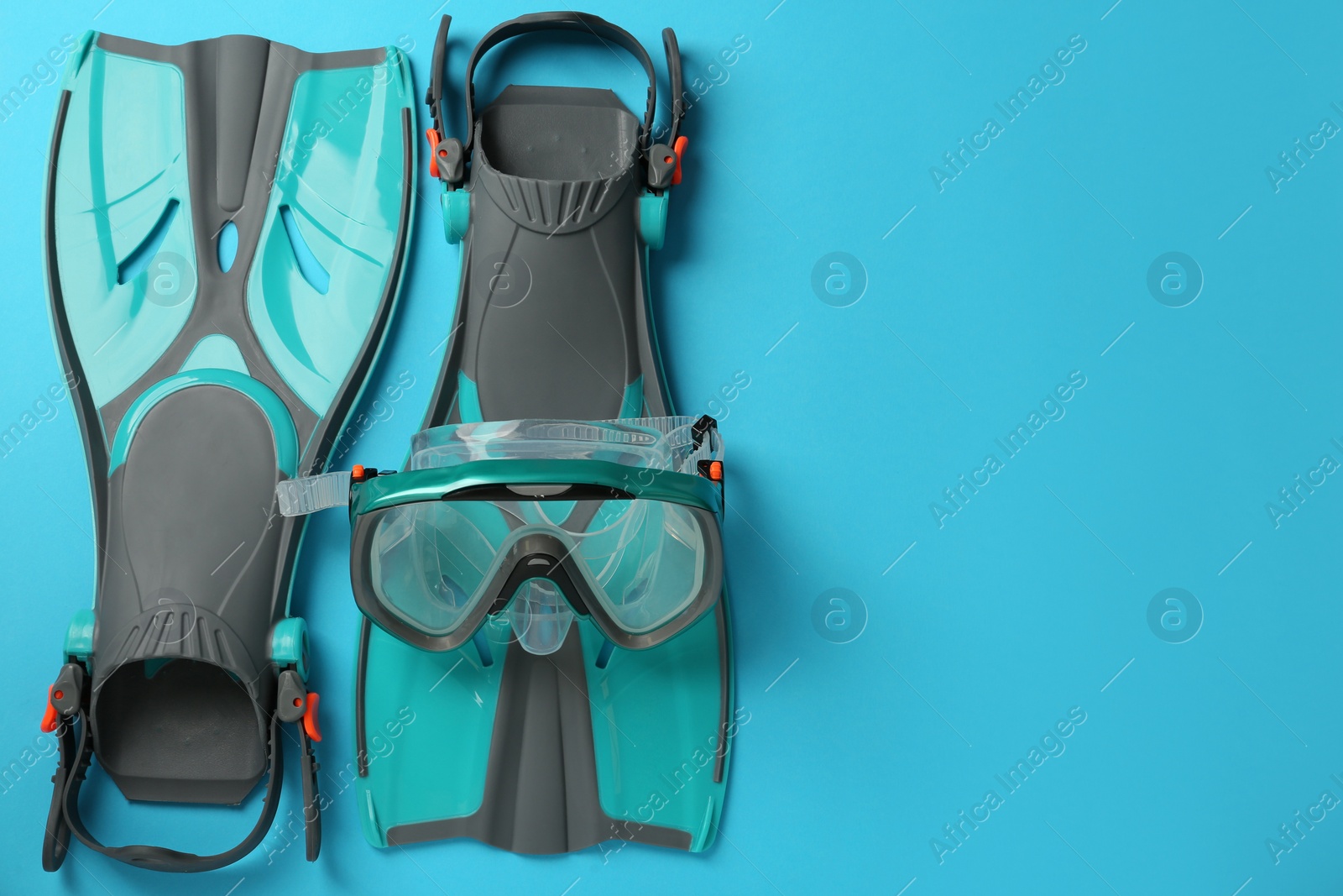 Photo of Pair of turquoise flippers and mask on light blue background, flat lay. Space for text