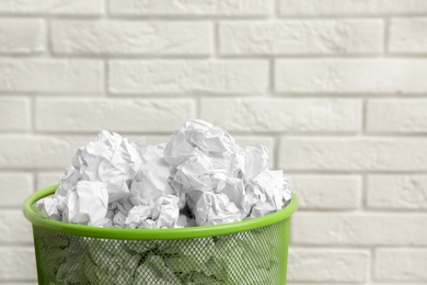 Photo of Metal bin with crumpled paper against brick wall, space for text