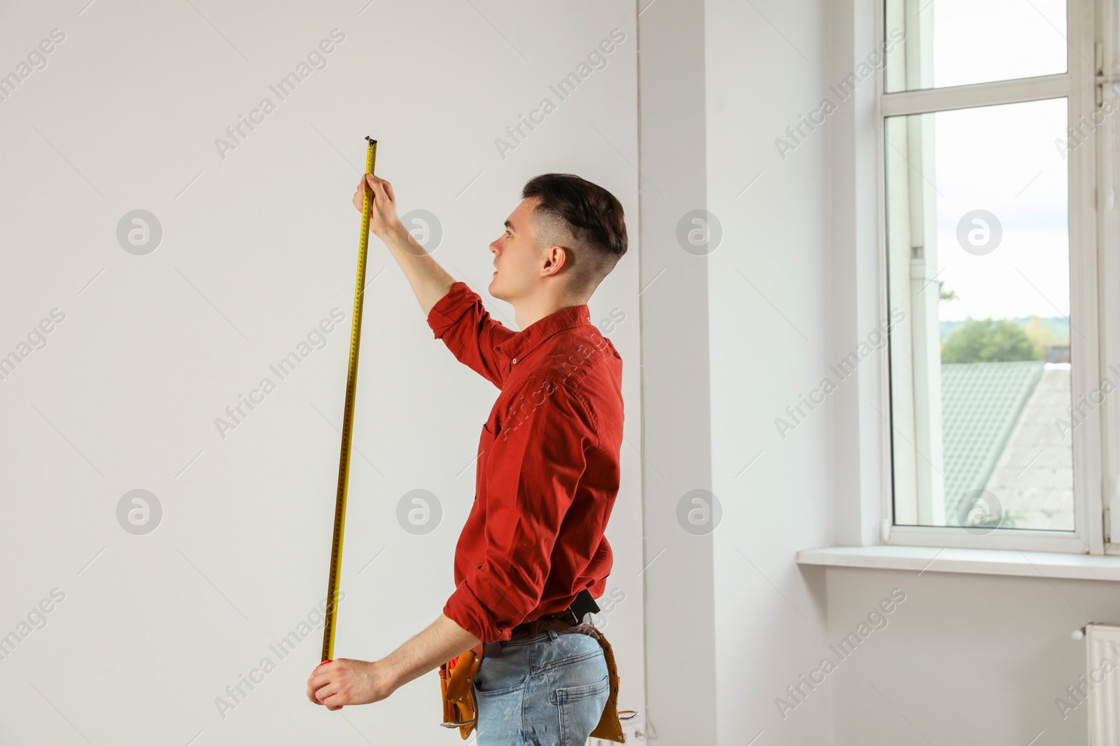 Photo of Handyman with toolbelt and measuring tape working in empty room