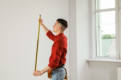 Handyman with toolbelt and measuring tape working in empty room