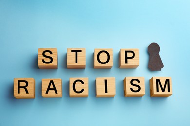 Photo of Black paper figure and wooden cubes with phrase Stop Racism on light blue background, flat lay