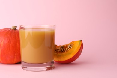 Photo of Tasty pumpkin juice in glass, whole and cut pumpkins on pale pink background, space for text