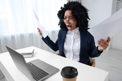 Photo of Deadline concept. Scared woman holding documents and looking at laptop in office