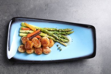 Photo of Delicious fried scallops with asparagus and vegetables on grey table, top view
