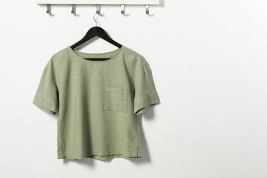 Hanger with olive t-shirt on white wall, space for text
