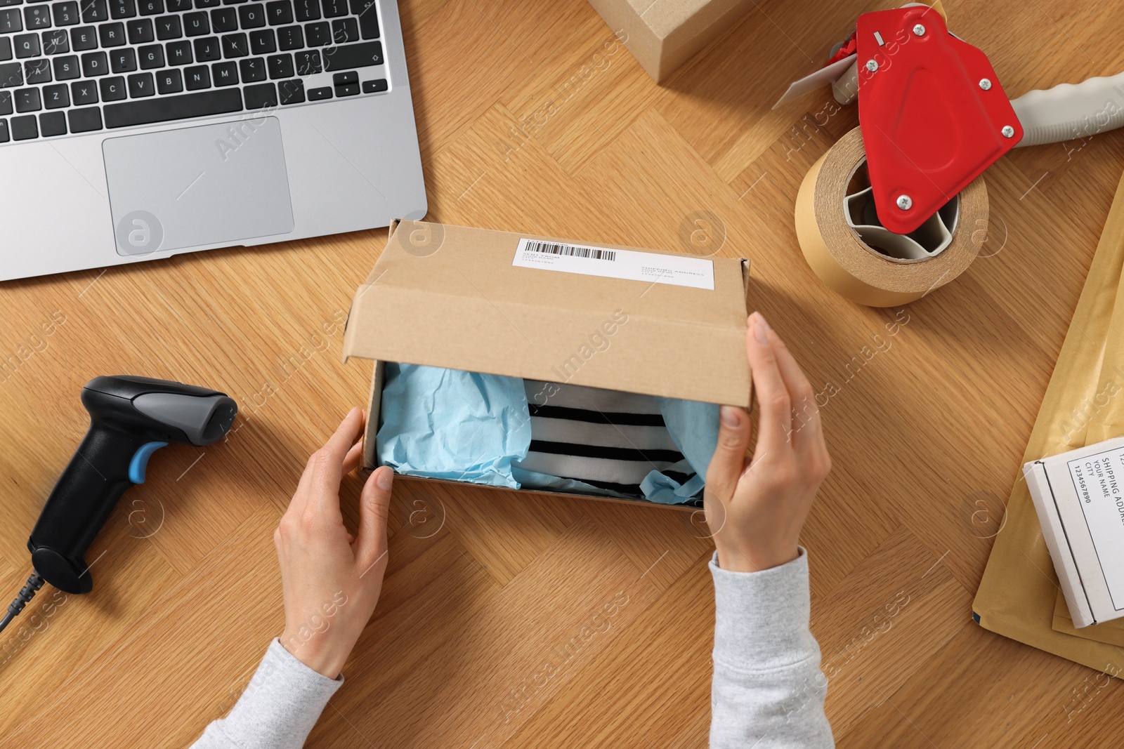 Photo of Woman packing clothes at wooden table, top view. Online store