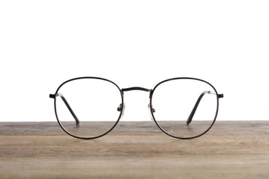 Photo of Stylish glasses with metal frame on wooden table against white background